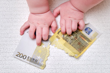 Baby hand and torn money in euros, close-up. Children fingers and an object on a white backgroundの写真素材