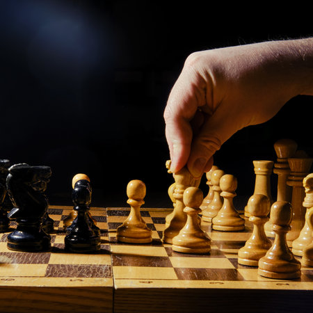 Player hand with a chess piece in a board game. Opening of the chess game, copy space on a black backgroundの写真素材