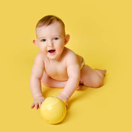 Happy toddler baby plays laughing on studio yellow background. Funny child boy sits and smiling, copy spaceの写真素材