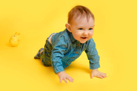 A happy child on a studio yellow background in a blue shirt and pants. Smiling infant baby boy in jeansの素材 [FY310183990187]