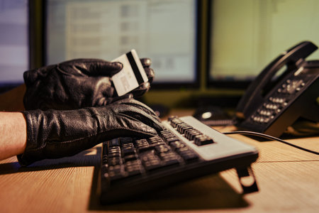 A man in black gloves with a plastic credit card in his hands at a computer keyboard in a dark night...