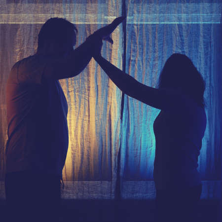 Silhouette of fighting man and woman at night window, domestic violence concept. Couple husband and wife having relationship problems in the evening light of the home living roomの写真素材