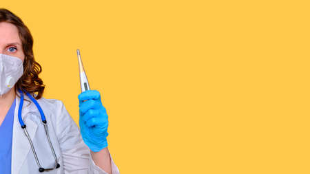 Doctor in a white uniform with a electronic thermometer in his hand on a yellow background, banner copy spaceの写真素材