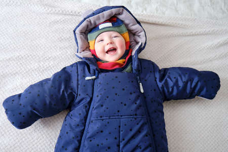 Happy baby boy dressed in warm winter clothes is lying on the bedの写真素材