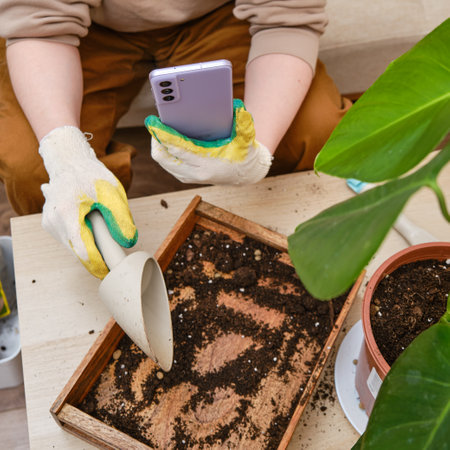 A woman gardener holds a Samsung S21 phone in her hands for online learning about plants. Blogger takes video and photo while working in home garden for internet blog - Moscow, Russia, March 24, 2022のeditorial素材