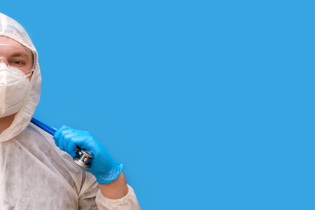 Doctor in a protective suit uniform with goggles and medical face mask on a studio blue background,...