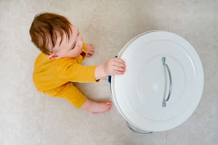 Toddler baby boy opens a trash can with household waste. Children's safety issues in the home room, little kidの写真素材