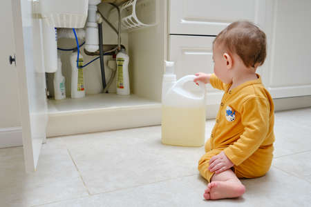 Toddler baby boy is playing with detergents and cleaning products in an open kitchen cabinet. Child safety issues in the home room, little kidの写真素材