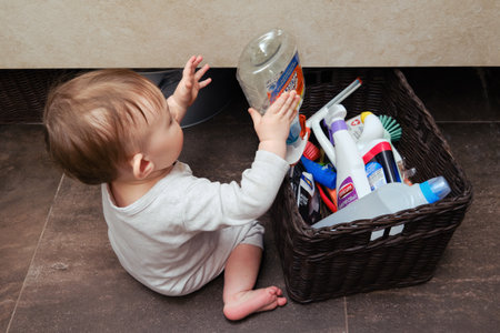 Toddler Baby Boy is playing in the toilet room with Mr. Muscle cleaning detergents. Child plays on a brown floor in a beige bathroom with household chemicals - Moscow, Russia, April 15, 2022のeditorial素材