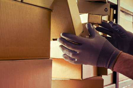 A worker man hands hold cardboard boxes on the shelves of a fully stocked warehouse. Warehouse overflowing with boxes of goods and postal parcelsの写真素材