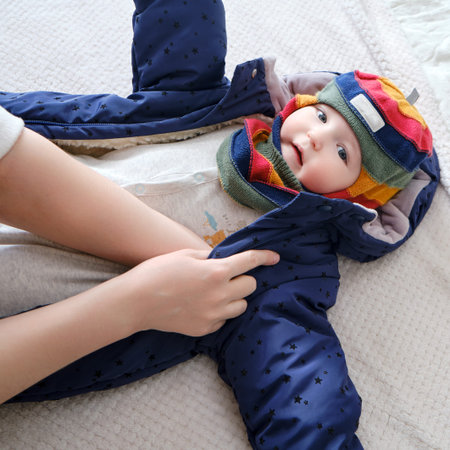 A mother woman puts on a warm jacket for a baby boy. Mom dresses a happy child in winter clothes on...