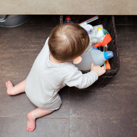 Toddler baby boy is playing in the toilet room with cleaning detergents. Child plays on a brown...