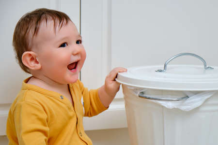 Toddler baby boy opens a trash can with household waste. Children's safety issues in the home room, little kidの写真素材