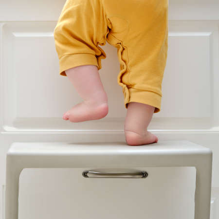 Toddler baby boy climbed with his feet on a high chair to climb on the kitchen cabinet. Child safety issues in the home room, little kidの写真素材
