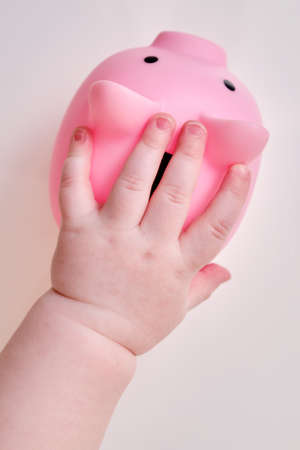 Baby hand and pink piggy bank, close-up. Children fingers and an object on a white backgroundの写真素材