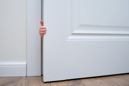 Toddler baby boy holds the edge of the open door with his hand. Close-up child hand at the door jambの写真素材