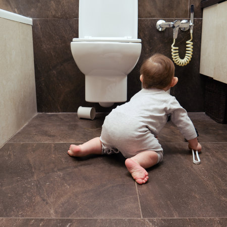 Toddler baby boy is playing in the toilet room with a brush. Child plays on the brown floor in the beige bathroomの写真素材
