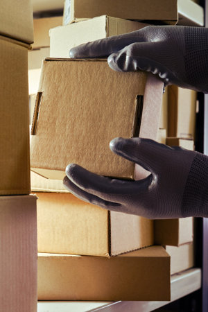 A worker man hands hold cardboard boxes on the shelves of a fully stocked warehouse. Warehouse...
