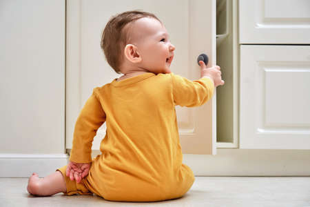 Toddler baby boy rips off a cabinet drawer with his hand. The child holds the cabinet door handle, small kidの写真素材