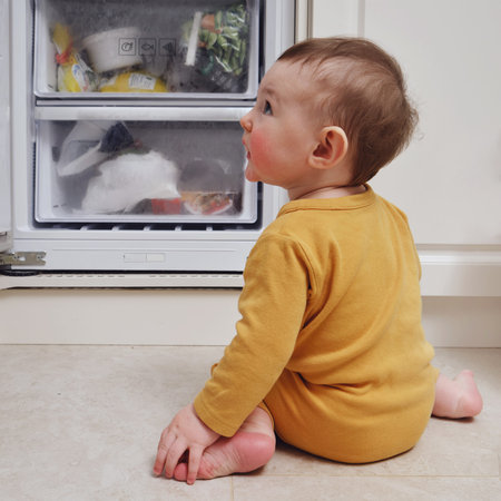 Toddler baby boy with allergies on red cheeks climbed into an open refrigerator. Child safety issues...