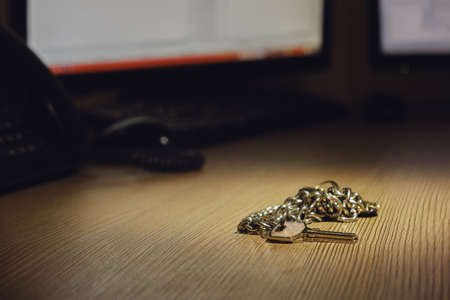 A bunch of keys to the room lies on an office desk with computer monitorsの写真素材