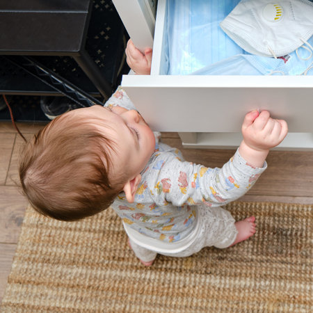 Toddler baby boy rips open a drawer of a closet full of medical face masks during the virus...
