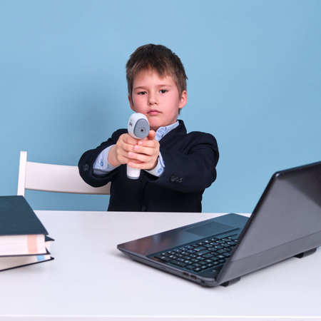 A boy in a school suit with a thermometer in his hands on distance learning, copy space on a blue...
