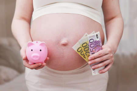 Euro money in the hands of a pregnant woman, home living roomの写真素材