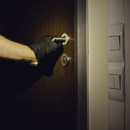 Man hand in a black glove opens the office door in the night light of a flashlightの写真素材