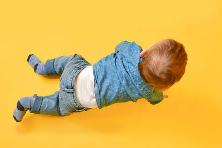 A happy child on a studio yellow background in a blue shirt and pants. Smiling infant baby boy in jeansの写真素材