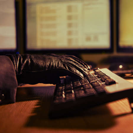 Man attacker hacker in black gloves on his hands working on a computer keyboard at an office desk, close-upの写真素材