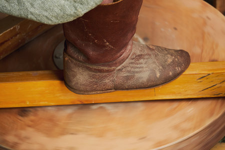 A man in old medieval Byzantine clothes sits behind a vintage potter's wheel and makes dishes out of...