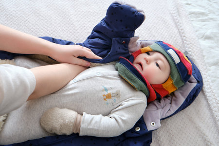 A mother woman puts on a warm jacket for a baby boy. Mom dresses a happy child in winter clothes on...