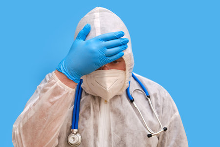 Man doctor medic in a protective suit uniform with goggles and face mask on a studio blue...