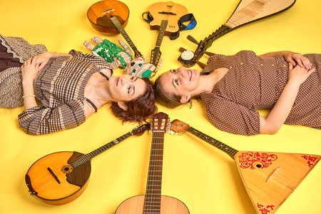 Women musicians in dresses with musical instruments on a yellow studio background. Happy artists...