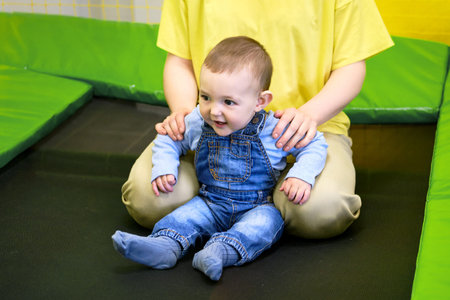 Happy toddler baby boy jumps on a trampoline with his mother in the playroom. Kid age one year