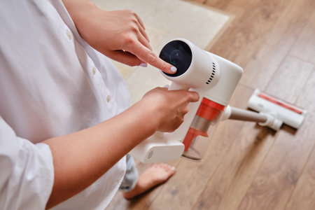Women hands and display control wireless portable vacuum cleaner in the kitchen. A woman cleans the floor in an apartment with a vacuum cleaner with a batteryの写真素材