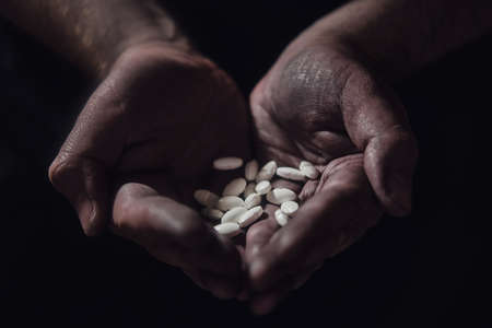 Pills in the dirty hands of a poor man on a black background. Hands of a person in need of treatment on a dark backgroundの写真素材