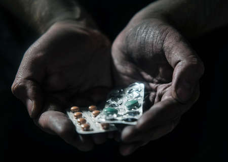 Pills in the dirty hands of a poor man on a black background. Hands of a person in need of treatment on a dark backgroundの写真素材