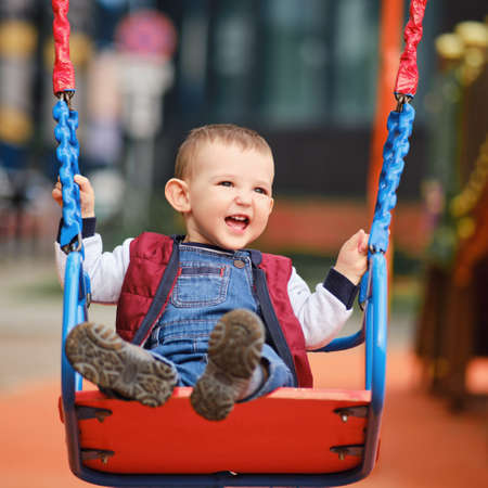 Happy toddler baby boy rides on a swing. Smiling child swinging on the playground, kid aged one yearの写真素材
