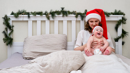 A happy woman with a smiling infant baby on a bed decorated for Christmas on New Year Eveの写真素材