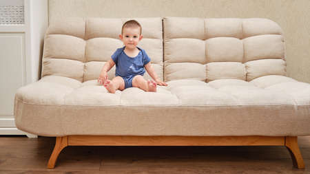 Toddler baby climbs on the sofa. Child boy learning to get off the bed. Kid age one yearの写真素材