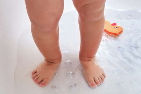 Toddler baby legs is standing on a non-slip mat in the bathtub. Child boy foot washes on the anti slip carpet in the bathroom. Kid age one yearの写真素材