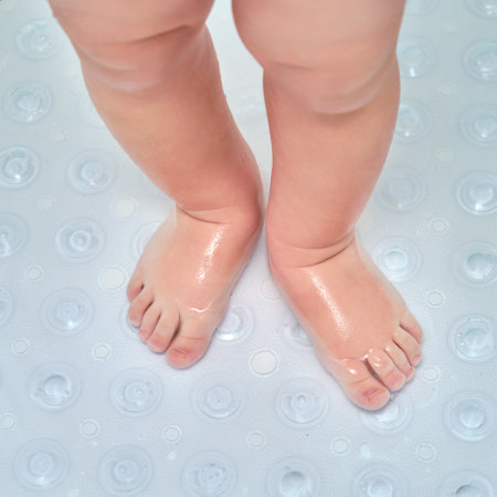 Toddler baby legs is standing on a non-slip mat in the bathtub. Child boy foot washes on the anti slip carpet in the bathroom. Kid age one yearの写真素材