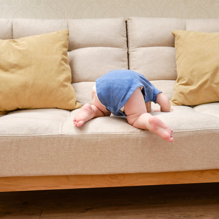 Toddler baby climbs on the sofa. Child boy learning to get off the bed. Kid age one yearの写真素材