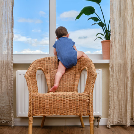 Toddler baby climbs to the window on the windowsill. Child crawls to the window holding on to the furniture in the home living room. Kid age one yearの写真素材