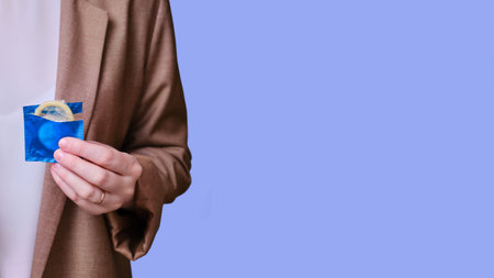 Woman teacher holding a condom in her hands on a blue background, banner close-up