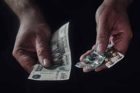 Money in Russian rubles and pills in the hands of a man on a black backgroundの写真素材