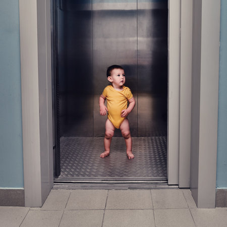 Toddler baby boy stands alone in the elevator of a residential building. A child in an elevator with...