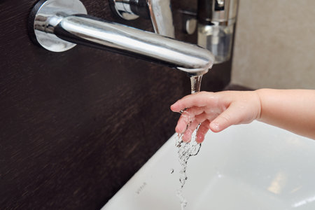 Toddler baby hand is washed under running water from the tap in the sink. Child learns to wash his handsの写真素材